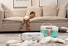 Un bebé en casa, cómodo, usando únicamente su pañal Nunuū, jugando sobre un sillón y mirando hacia el piso de la sala donde se encuentran bolsas y pañales Nunuū