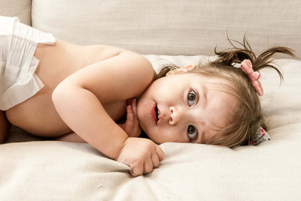 Una bebé jugando sobre un sillón con cara divertida de sorpresa.