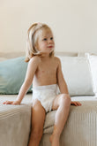Niña sentada sobre un sillón suave, usando el pañal Nunuū 