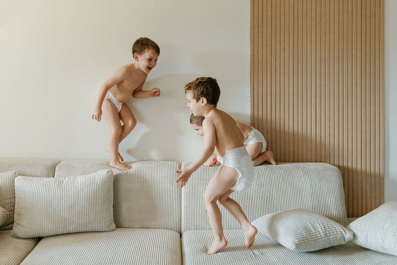 Tres niños usando pañal. Nunuū saltando y jugando sobre un sillón suave. 