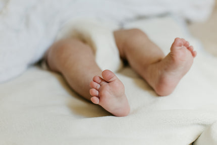 Los piecitos de un bebé acostado usando un pañal Nunuū. El resto de la imagen es desenfocada. 